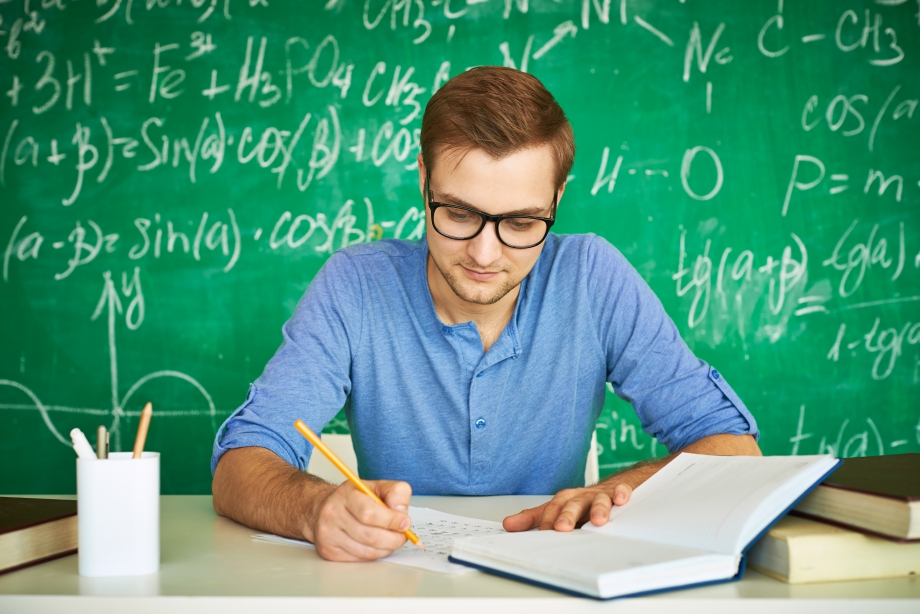 Portrait of handsome student carrying out graduation test on background of chalkboard