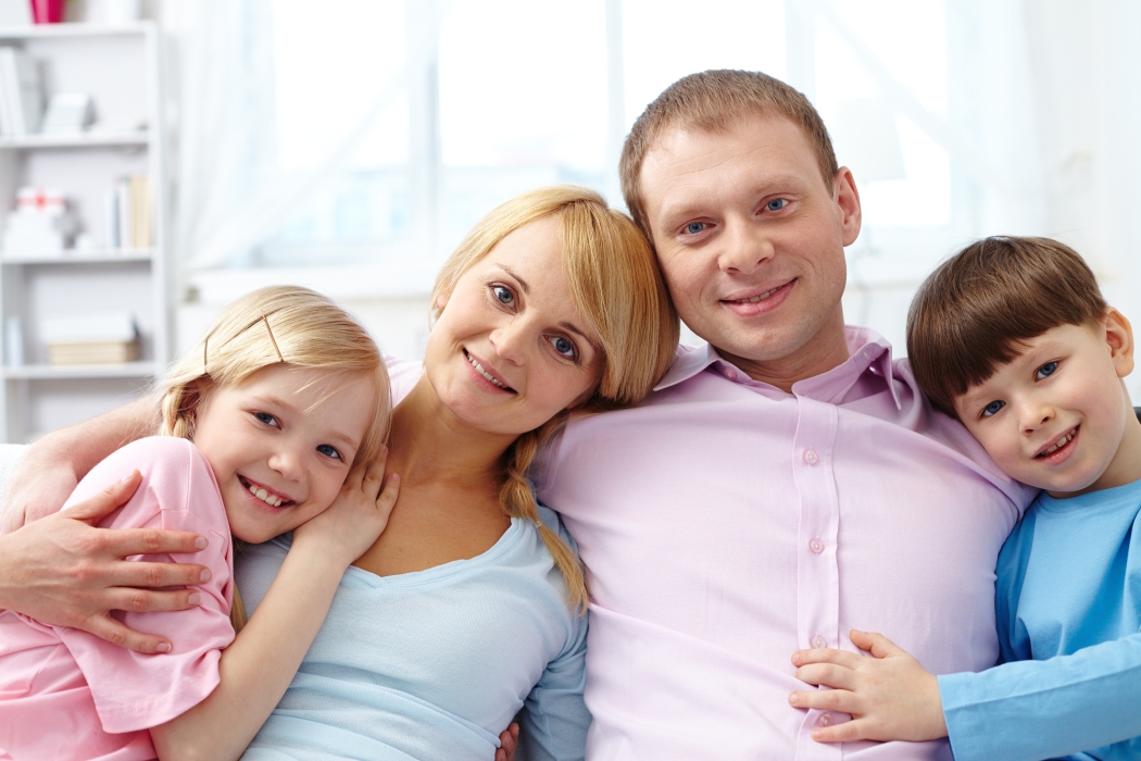 A young family of four looking at camera and smiling while relaxing at home